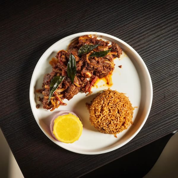 Paheli Modern Indian Cuisine's spicy beef fry with rice, lemon, and onions on a white plate.