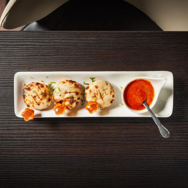 Three grilled Indian flatbreads with a side of red sauce and star-shaped garnishes on a white plate.