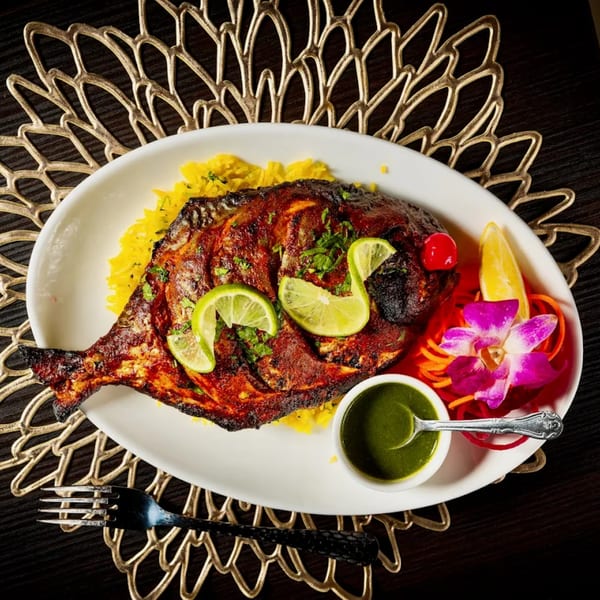 Whole grilled fish, garnished with lime, cilantro, and a side of green chutney, on yellow rice.