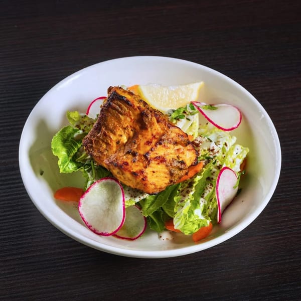 Grilled Indian salmon with fresh salad, radish, and a lemon wedge in a white bowl.